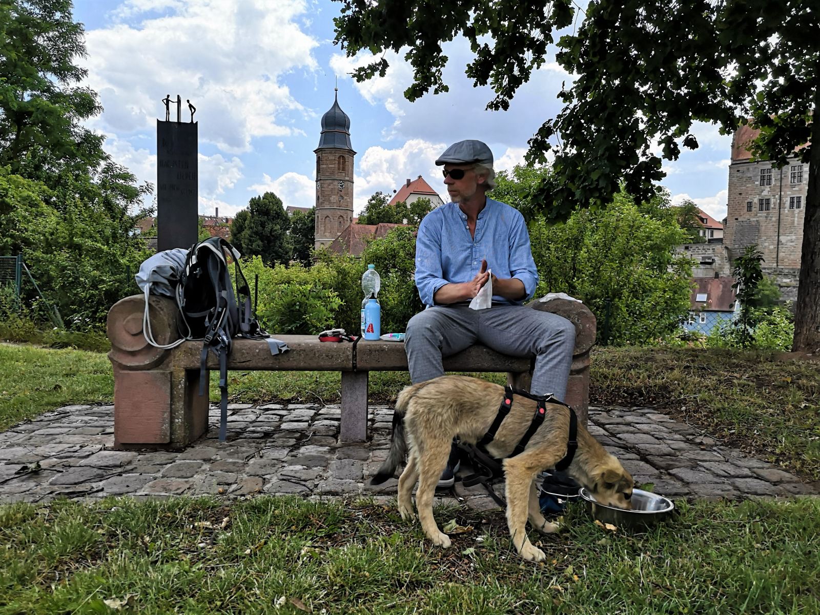 Ein mann mit Welpe macht Pause auf einer Bank. Der Hund trinkt gerade.