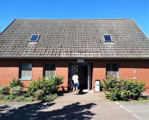 Eine Frau wartet mit ihrem Hund vor der Touristeninformation im Hafen von Altwarp.