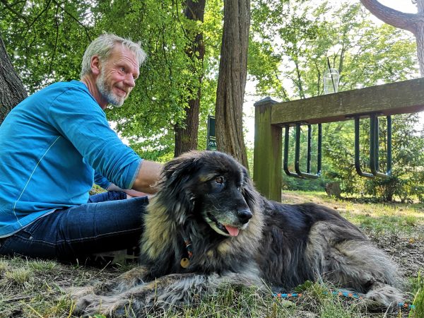Ein Mann und sein Hund sitzen auf einer Wiese.