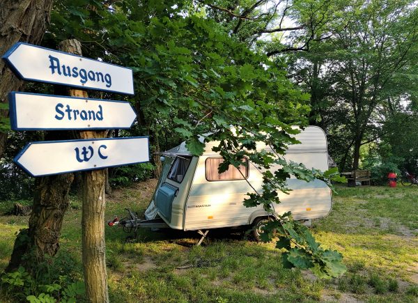 Ein kleiner Wohnwagen steht auf einem Campingplatz am See.