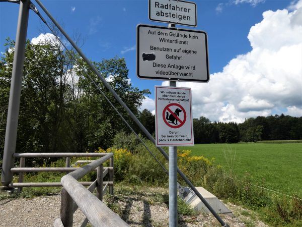 Ein Hinweisschild am Flussufer bittet darum, Hundekot einzusammeln.