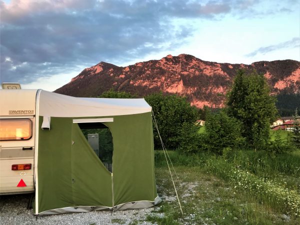 ein grünes Vorzelt steht in einer Wiese vor einem Hügel