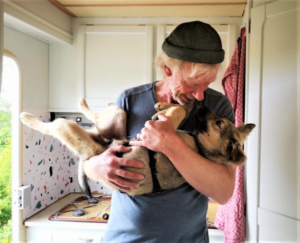 Ein Mann mit Mütze hält einen kleinen Hund im Arm