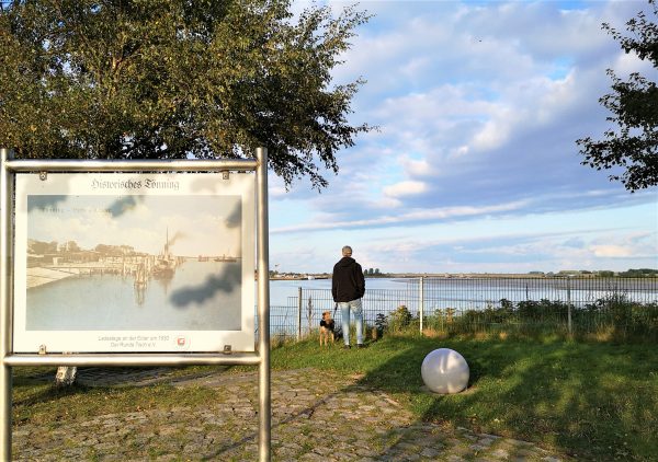 Ein mann mit Hund steht am Ufer und blickt über das Wasser